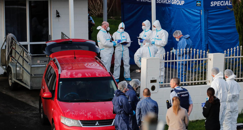 Police investigators wearing white jumpsuits stand outside the home in Manurewa where the bodies were found 