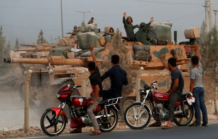 People wave as Turkish military vehicles pass by them in the Turkish border town of Akcakale in Sanliurfa province