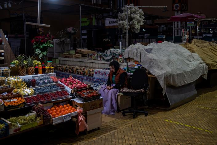 A fruit vendor waits for customers inside a dark market in downtown Kyiv, Ukraine, Monday, Nov. 7, 2022. The city is struggling to keep the lights on amid Russian assaults on the electrical grid.