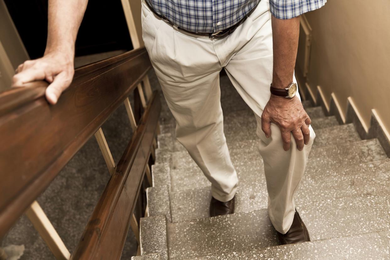 senior walking up stairs in a walkup, with hand on knee because of pain