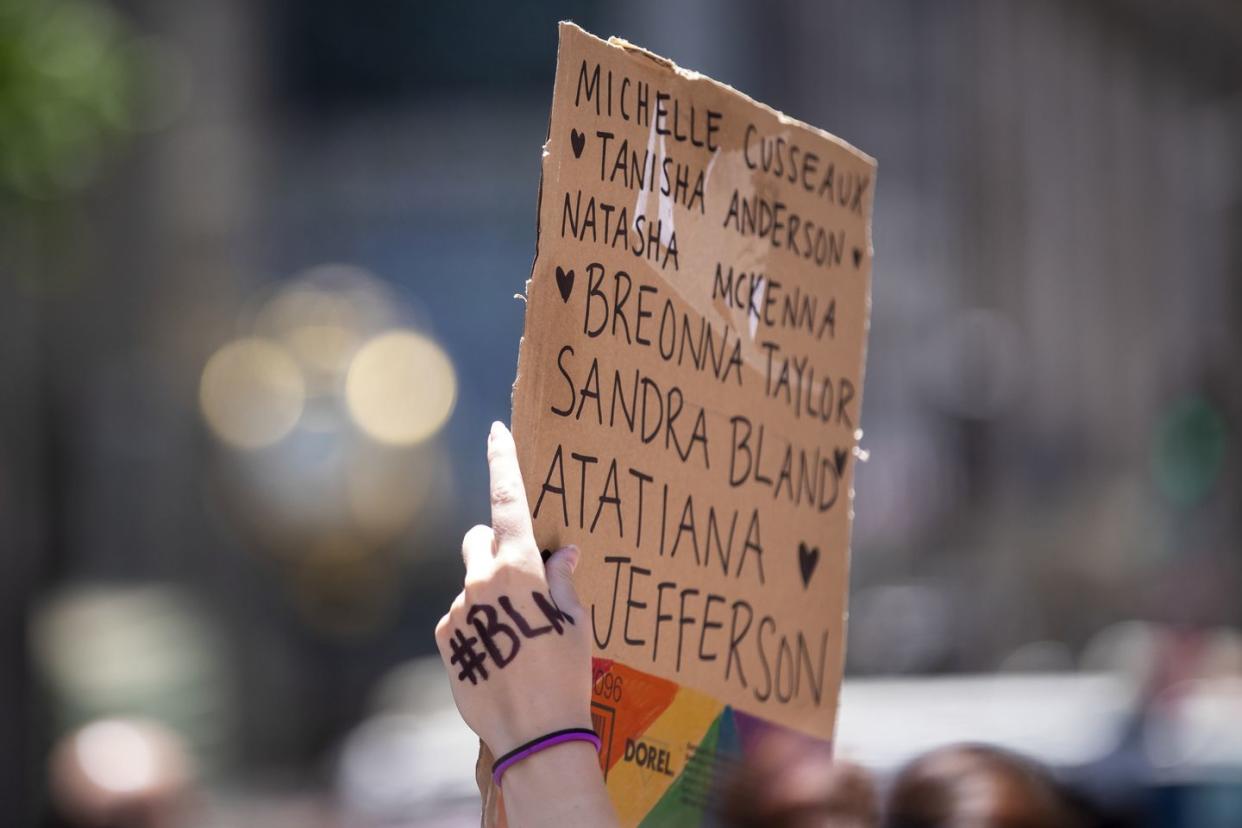 a protester holds up their homemade sign on a box that says, breonna taylor, atatiana jefferson, sandra bland natasha mckenna, tanisha anderson, michelle cusseausx with the letters blm written on their hand and the rainbow colors on the box during a protest at trump tower