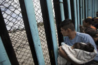 <p>A member of the Central American migrant caravan, holding a child, looks through the border wall toward a group of people gathered on the U.S. side, as he stands on the beach where the border wall ends in the ocean, in Tijuana, Mexico, April 29, 2018. (Photo: Hans-Maximo Musielik/AP) </p>