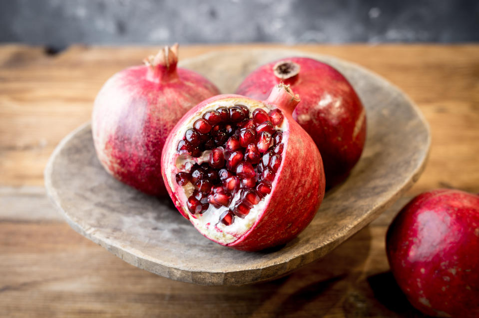 Three pomegranates on a rustic wooden plate, one half-open to reveal the seeds.