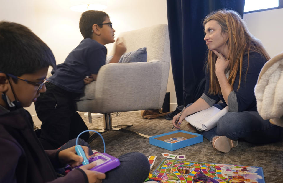 Therapist Sarah Sutton, right, listens to an animated Keaton Kotiya, 9, as is brother Ronan Kotiya, 11, sits and listens during a counseling session in Plano, Texas, Friday, April 8, 2022. Caregiving for their father with ALS is a task that children like Ronan and Keaton take seriously and something that their mom hopes will shape them into empathetic, strong young men. But getting there first involves a daily struggle to balance being a kid with living in a very grown-up world. Sutton has seen the boys regularly for a few years. She's been trying to get them to recognize all the emotions hitting them and realize where they are coming from instead of keeping everything bottled up. (AP Photo/LM Otero)