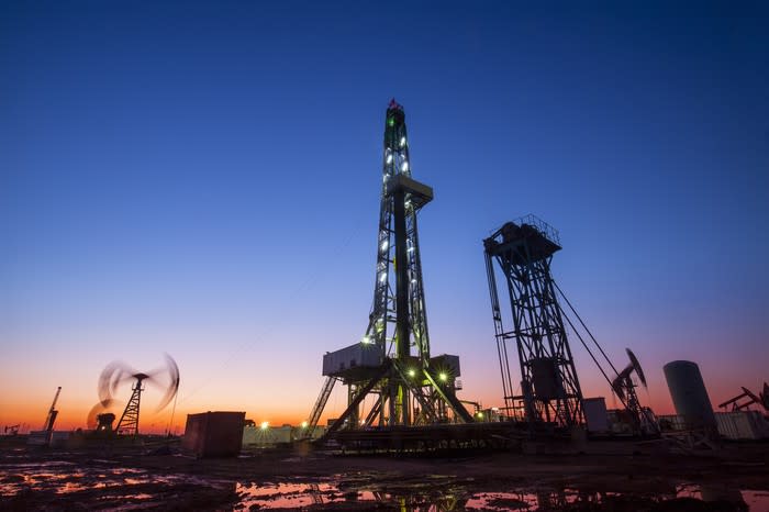 A drilling rig near a pump at dusk.