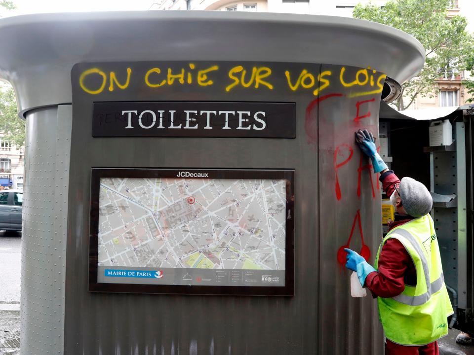 An employee cleans a public toilet which has been graffitied with the words 'We crap on your laws' in French