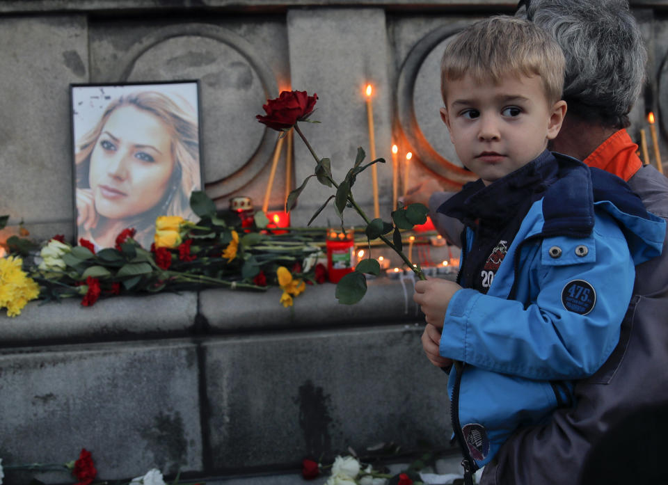 A child holds next to a portrait of slain television reporter Viktoria Marinova during a vigil at the Liberty Monument in Ruse, Bulgaria, Monday, Oct. 8, 2018. Bulgarian police are investigating the rape, beating and slaying of a female television reporter whose body was dumped near the Danube River after she reported on the possible misuse of European Union funds in Bulgaria. (AP Photo/Vadim Ghirda)