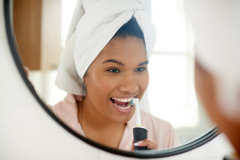 A woman uses an electric toothbrush to brush her teeth.