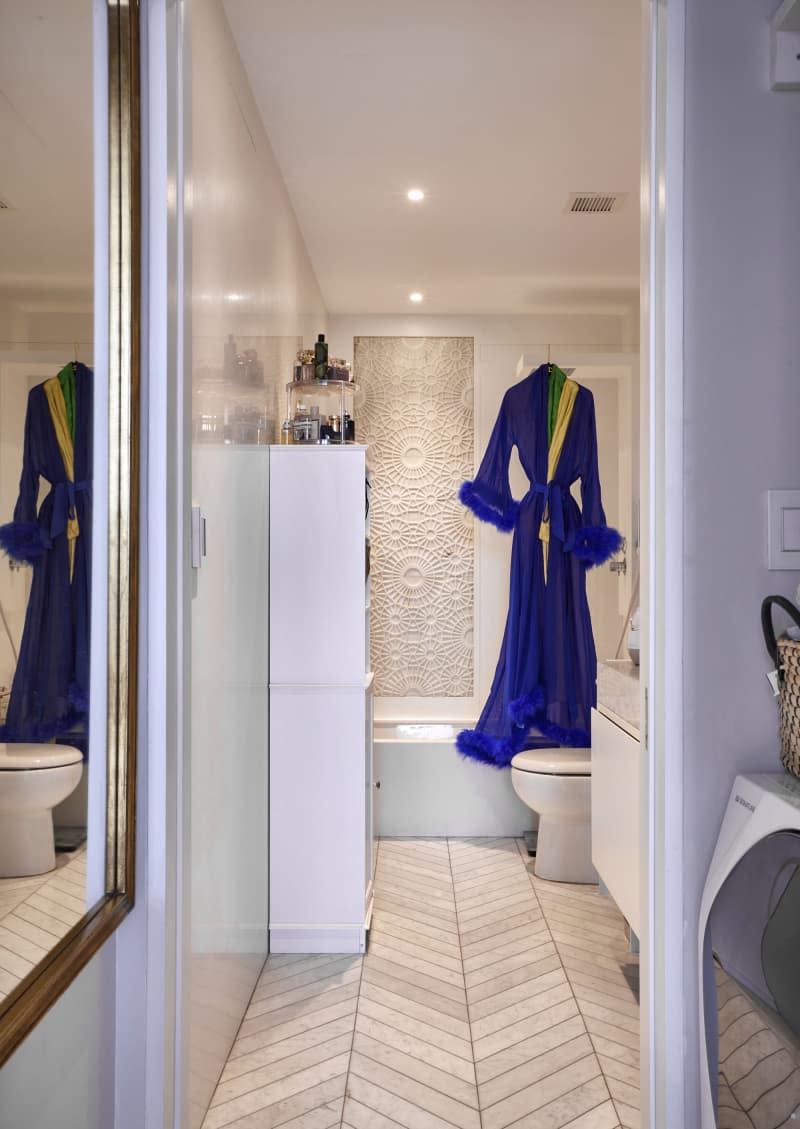 Bathrobe hanging in white bathroom with white herringbone floors.