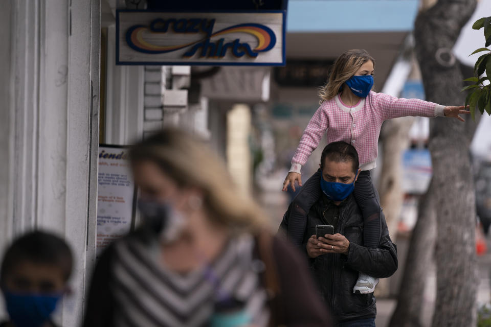 Bijan Parsi looks at his phone while carrying his daughter Ava, 6, on his shoulders in Laguna Beach, Calif., Monday, May 17, 2021. California won't lift its mask requirement until June 15 to give the public and businesses time to prepare and ensure cases stay low, state Health Director Mark Ghaly said Monday. (AP Photo/Jae C. Hong)