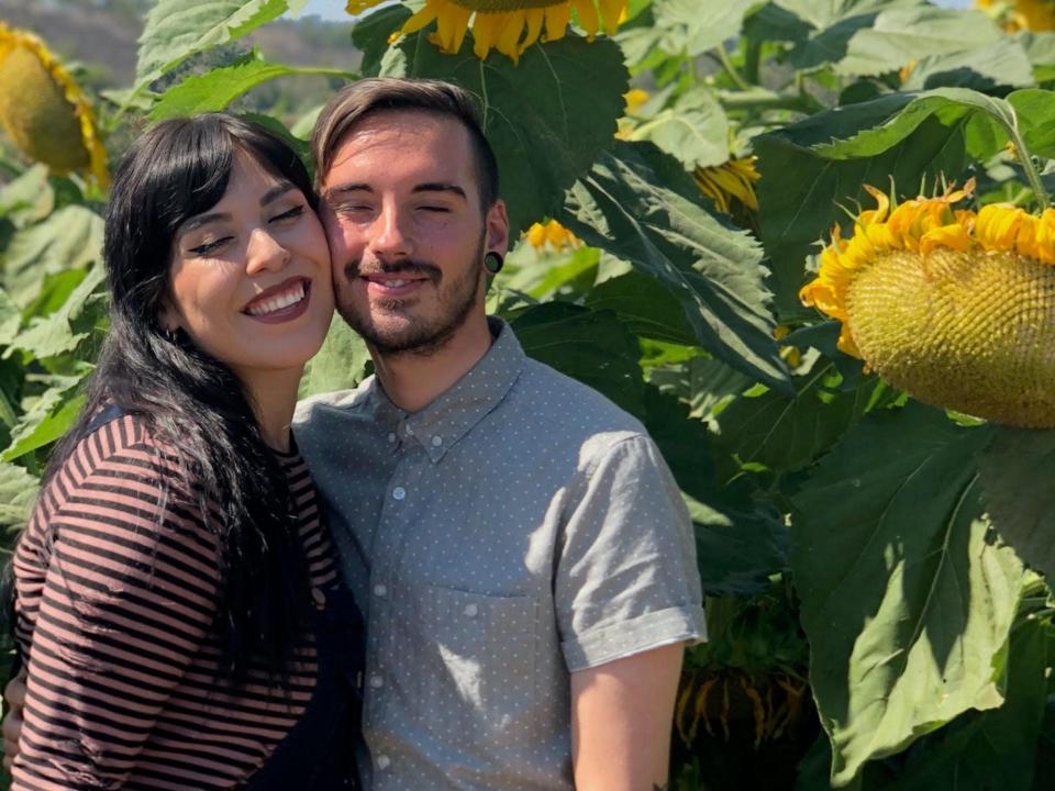 A couple pose for a photo under a large sunflower.