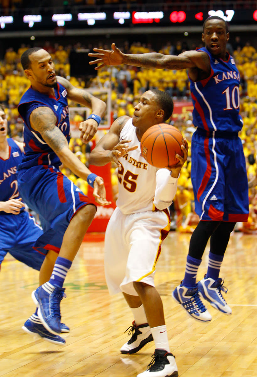 Iowa State guard Tyrus McGee (25) passes the ball between Kansas defenders Travis Releford, left, and Tyshawn Taylor, right, during second half of an NCAA college basketball game, Saturday, Jan. 28, 2012, in Ames, Iowa. Iowa State won 72-64.