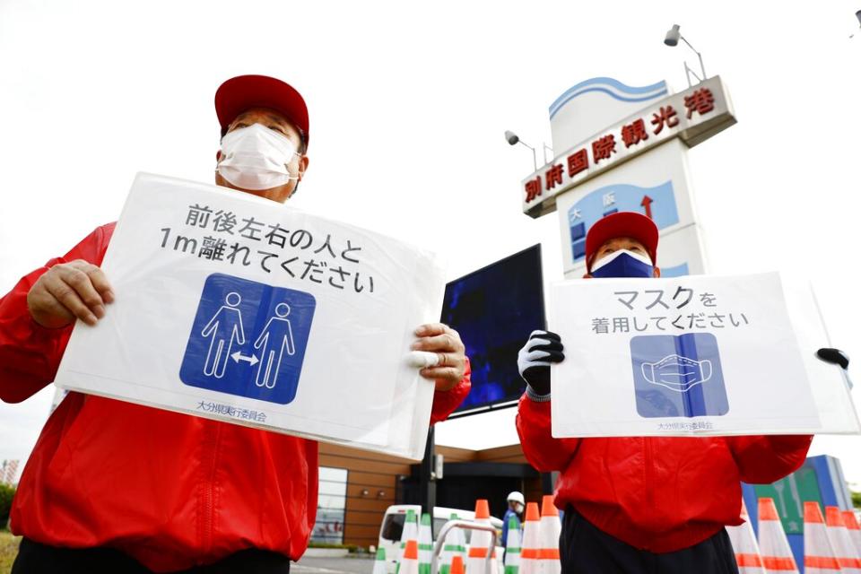Organizing staff members of the Tokyo Olympic torch relay hold signs urging spectators to wear masks and maintain social distancing in the Oita Prefecture city of Beppu, southwestern Japan, on April 23, 2021, amid the coronavirus pandemic.<span class="copyright">Kyodo News/AP Images</span>