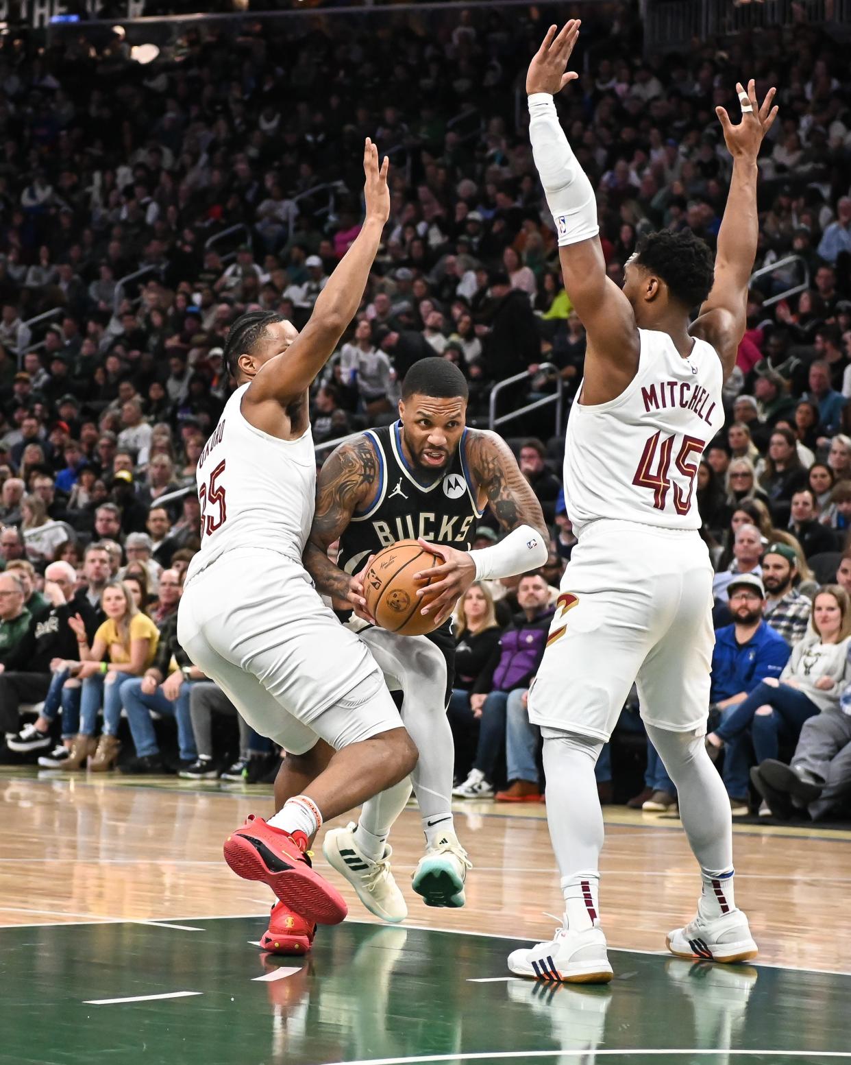 Milwaukee Bucks guard Damian Lillard (0) drives to the basket between Cleveland Cavaliers forward Isaac Okoro (35) and guard Donovan Mitchell (45) on Jan. 26 in Milwaukee.