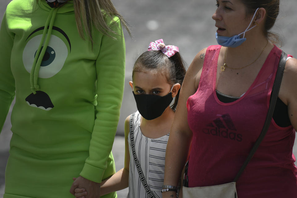 A child wearing a mask amid the new coronavirus pandemic walks with her mother and aunt on Sabana Grande boulevard in Caracas, Venezuela, Wednesday, June 17, 2020. (AP Photo/Matias Delacroix)