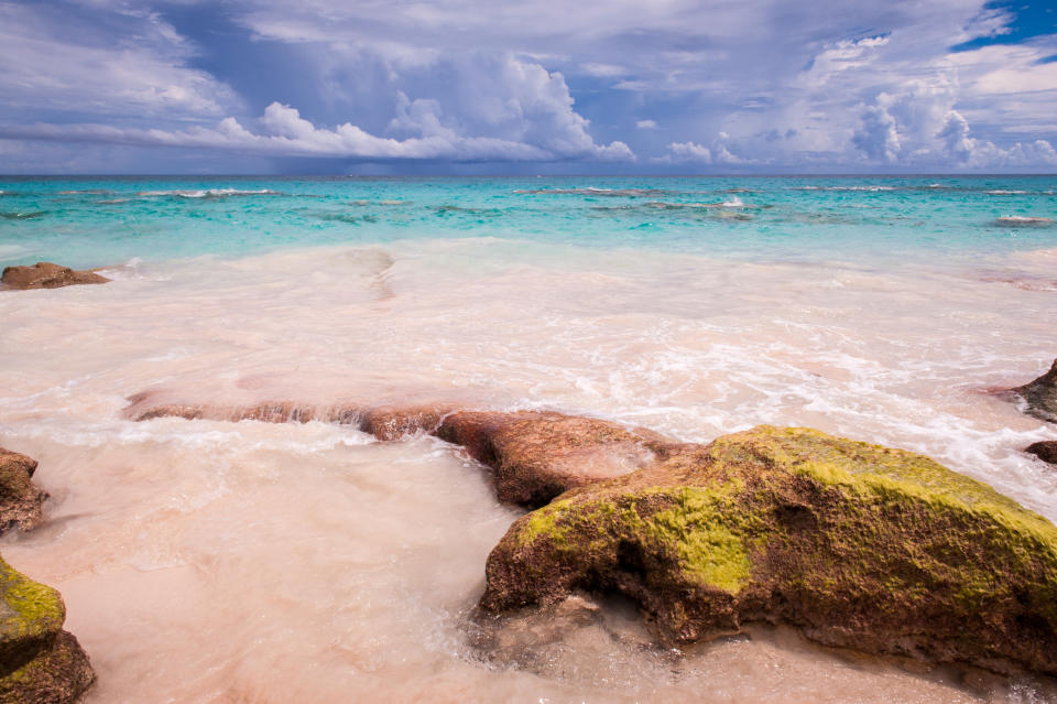 Famous deserted Horse shoe Bay beach with pink sand and rocks, Bermuda. Shot on a bright sunny day with some clouds in the sky and vibrant turquiose water.