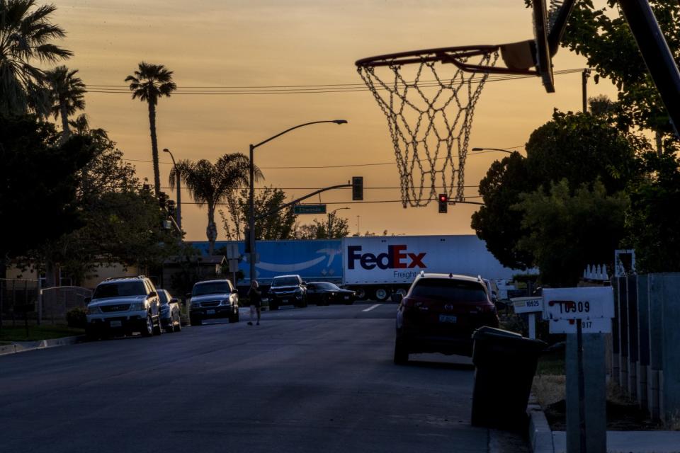Amazon and FedEx big rig trucks pass by a neighborhood in route to warehouses nearby off of Etiwanda Avenue