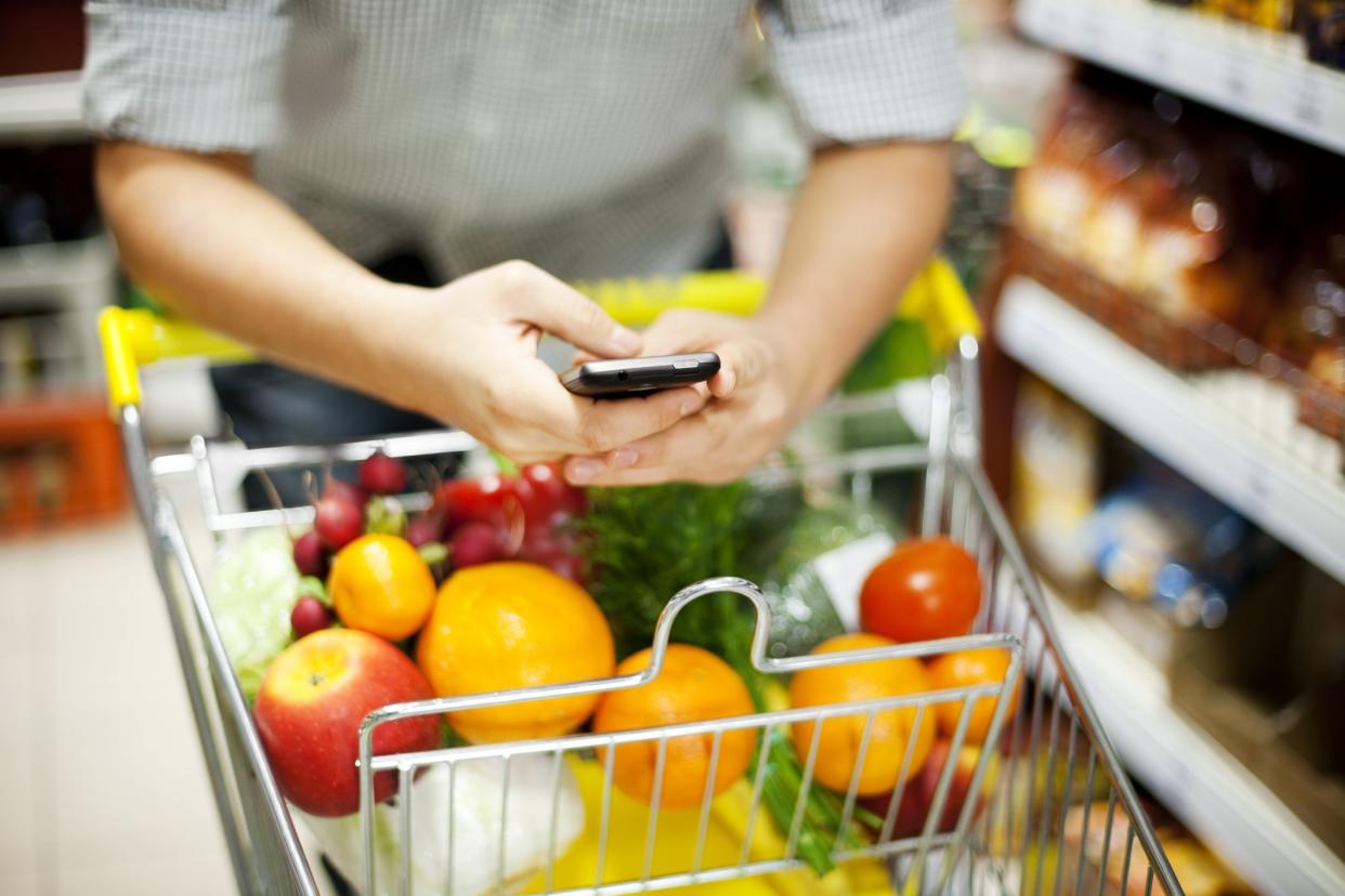 Man on phone while moving a shopping cart of food.