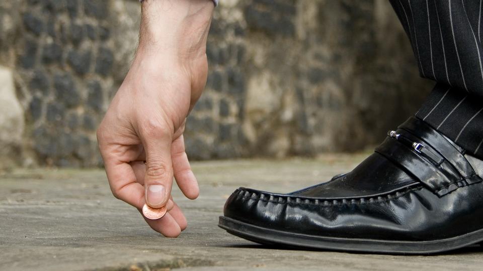 Businessman bending down to pick up a lucky penny.