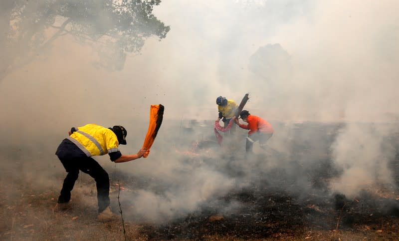 Residents try to knock down spot fires, from a bushfire, heading towards a house on a property at Koorainghat