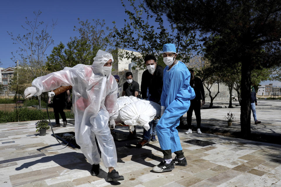 People wearing protective clothing carry the body of a victim who died after being infected with the new coronavirus at a cemetery just outside Tehran, Iran, Monday, March 30, 2020. The new coronavirus causes mild or moderate symptoms for most people, but for some, especially older adults and people with existing health problems, it can cause more severe illness or death. (AP Photo/Ebrahim Noroozi)