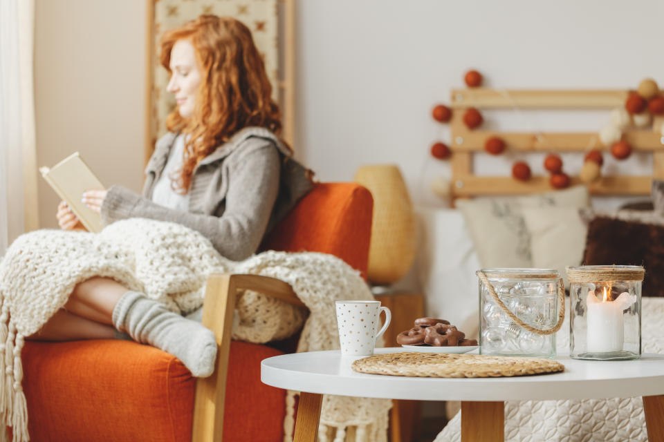Woman with red hair sitting on chair with blanket and surrounded by candles in a cozy space