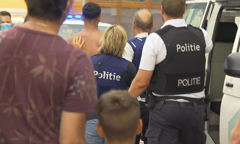 In image made from video provided by VTM, a man is detained by police, centre back, after a skirmish on the beach in Blankenberge, Belgium on Saturday, Aug. 8, 2020. It started as a Saturday trip to the coast, a chance to escape the heat wave that's settled over Belgium and forget coronavirus restrictions for a while. As the tide came in, the beach got crowded. Someone complained about the music being too loud. Things degenerated fast. Within minutes, dozens of people were battling it out on the sand, some throwing bottles and umbrellas at police. (VTM via AP)