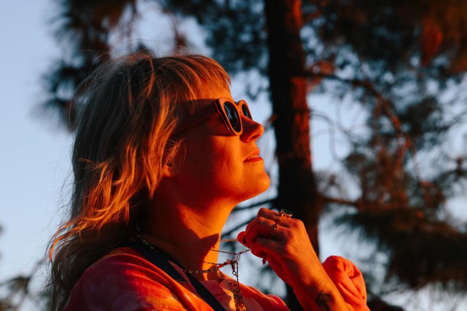 Lauren Powell listens to poetry readings at sunset sitting on the ground amid trees.