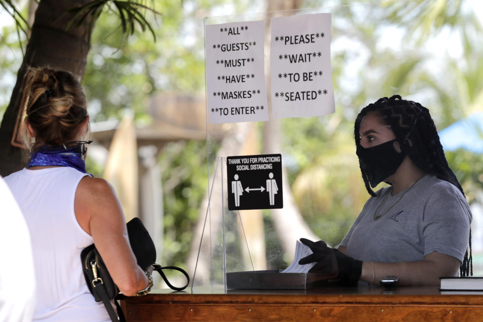 Nailea Rosales works behind a protective shield wearing a protective mask and gloves at the Morada Bay Beach Cafe in Islamorada, in the Florida Keys, during the new coronavirus pandemic, Monday, June 1, 2020. The Florida Keys reopened for visitors Monday after the tourist-dependent island chain was closed for more than two months to prevent the spread of the coronavirus. (AP Photo/Lynne Sladky)