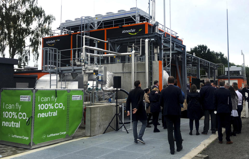 People are seen in front of the 'Atmosfair' synthetic kerosene plant in Werlte, Germany, Monday, Oct. 4, 2021. German officials are unveiling a facility in Werlte, near Germany's northwestern border with the Netherlands, what they say will be the world's first commercial plant for making synthetic kerosene as part of an effort to reduce the climate impact of flying. (AP Photo/Aleksandar Furtula)