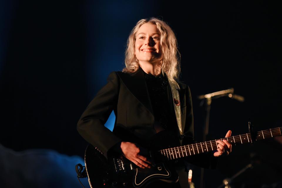 Phoebe Bridgers holds a guitar and smiles in an all-black outfit on Glastonbury stage