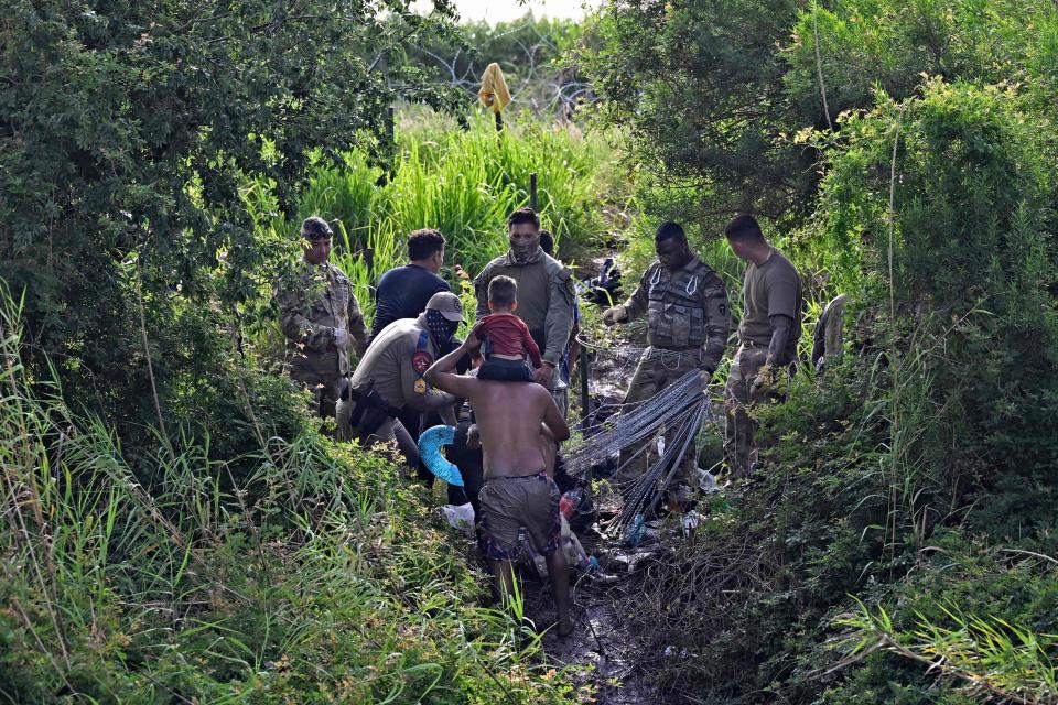 Migrants who crossed the Rio Grande River try to go through as members of the US National Guard put a barbed-wire fence along the US-Mexico border river, as seen from Matamoros, state of Tamaulupas, Mexico.