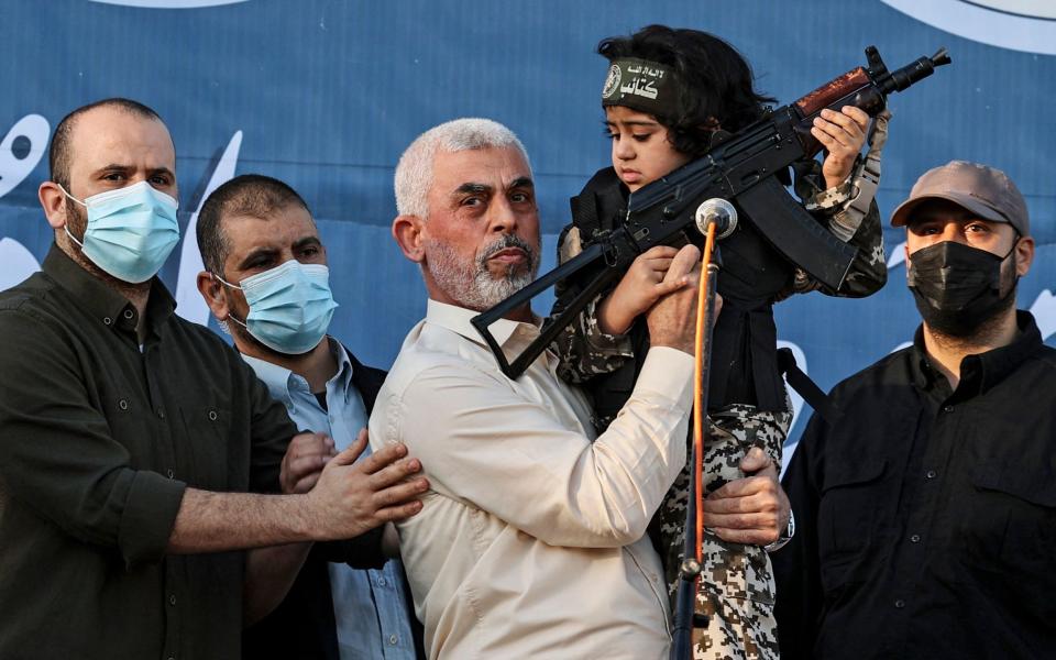 Sinwar holding a very small child who is himself holding a sub-machine gun