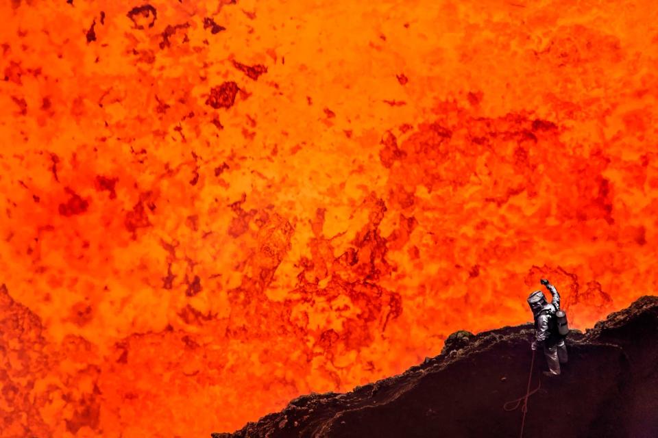 Geoff Mackley, wearing protective gear, looks down at 1,150 degree lava at the heart of the Marum Volvano, Vanuatu (Caters)