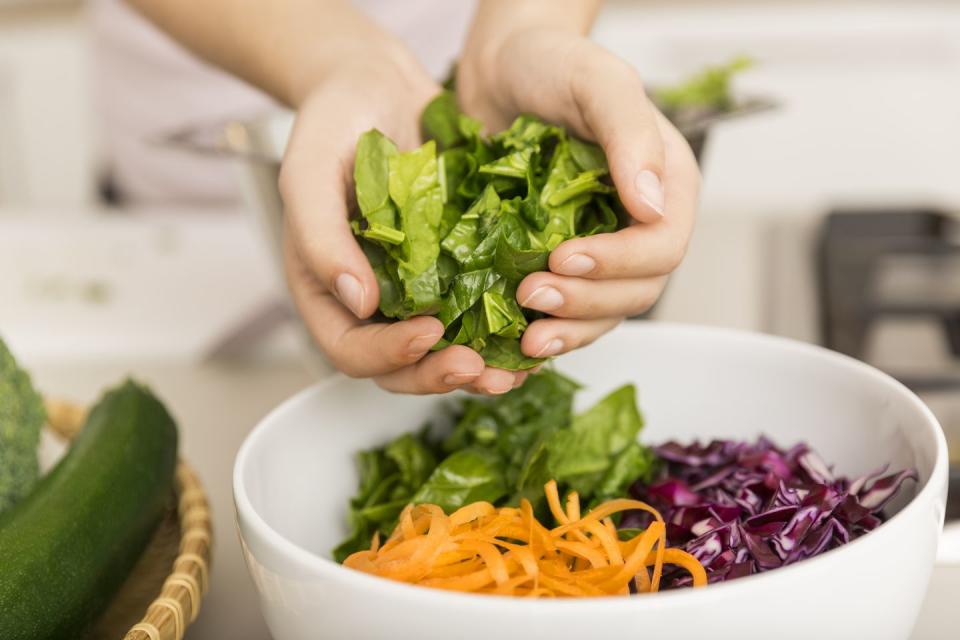 hands putting fresh lettuce into a bowl with different vegetables