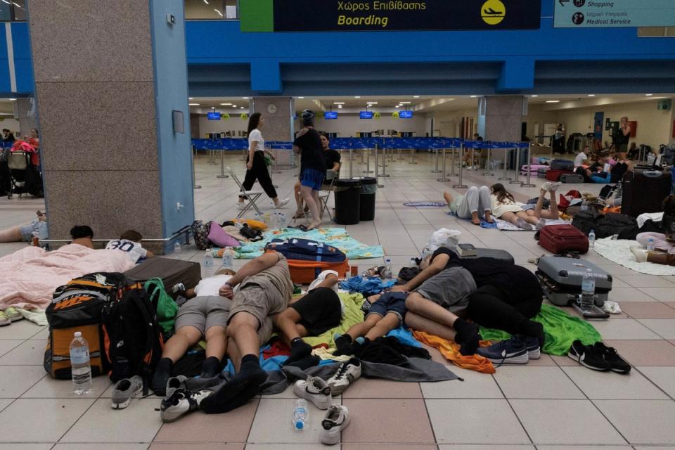 Tourists sleep as they wait for departing planes at the airport, after being evacuated following a wildfire on Rhodes on Monday morning (REUTERS)