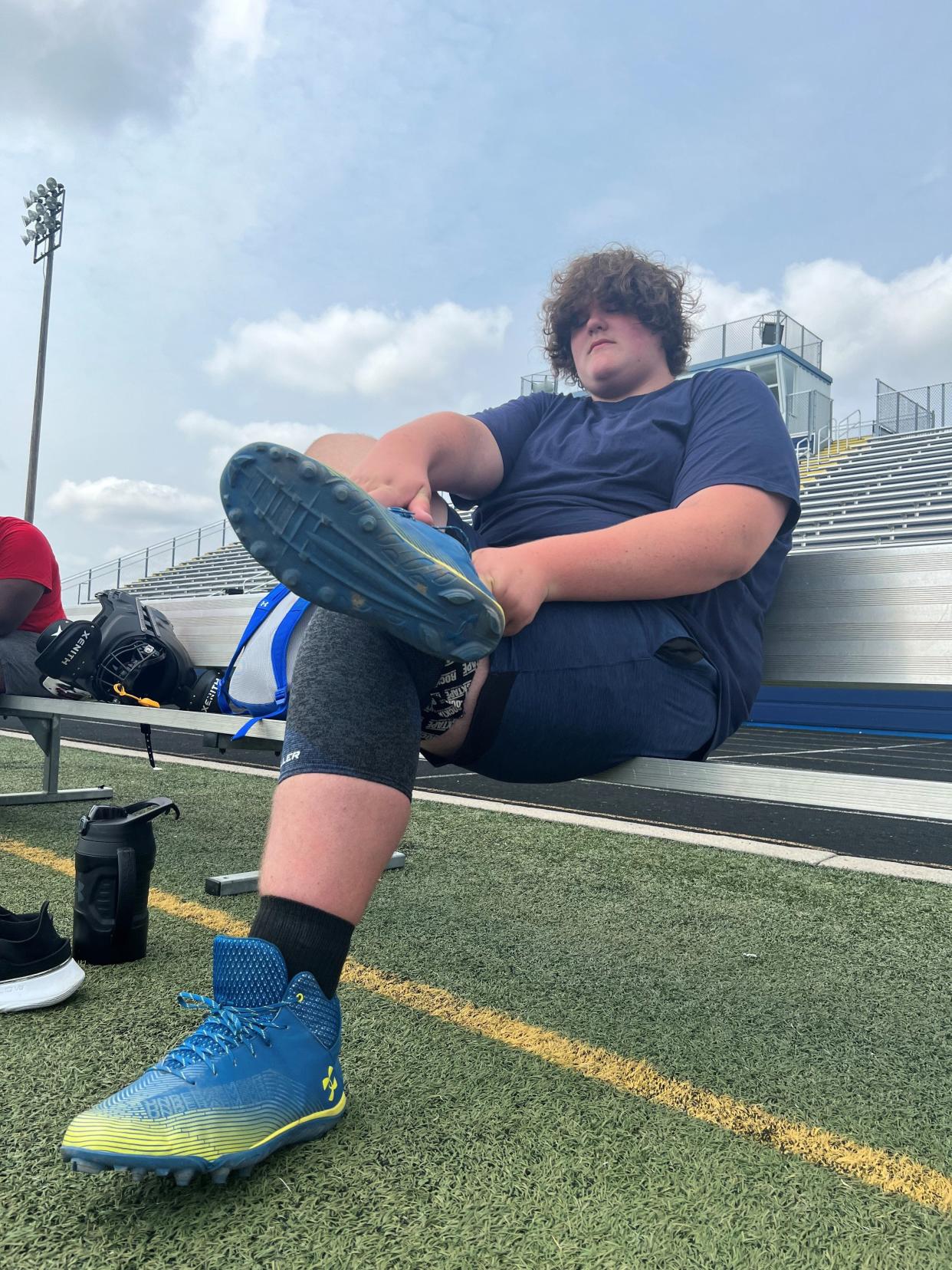 Eric Kilburn Jr., 15, puts on his new cleats, custom made by Under Armour, prior to JV football practice at Goodrich High School, Aug. 21, 2023. UA, which has never made cleats this large before, created the shoes after Eric had outgrown size 22.