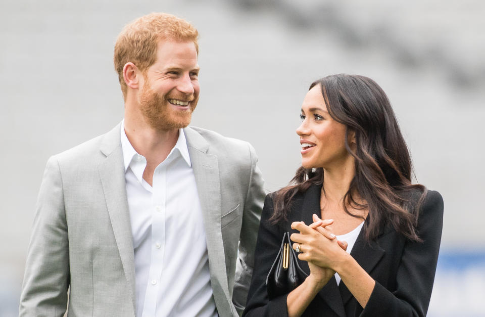 Prince Harry laughs as Meghan Markle looks at him wearing a black blazer