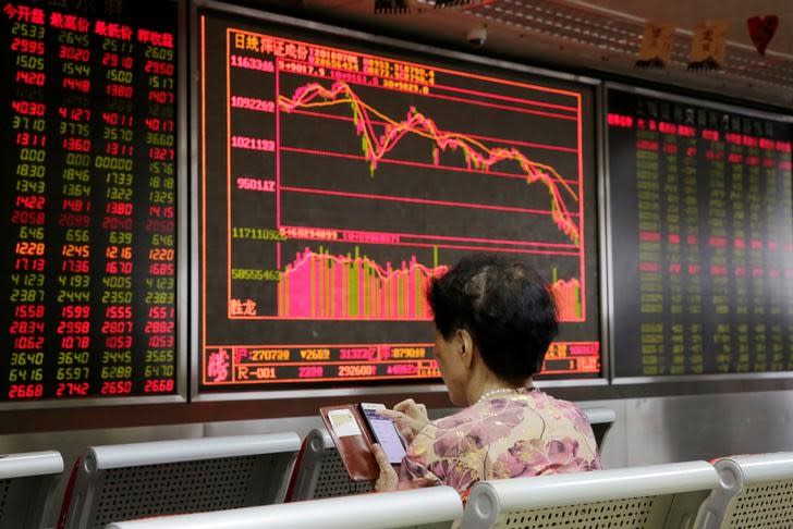 An investor checks stock information on her mobile phone in front of a board at a brokerage office in Beijing, China July 6, 2018. REUTERS/Jason Lee