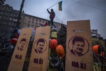 An anti-government protester wave the Ukrainian flag as he stands on fortifications against riot police in Kiev, January 28, 2014. REUTERS/Thomas Peter