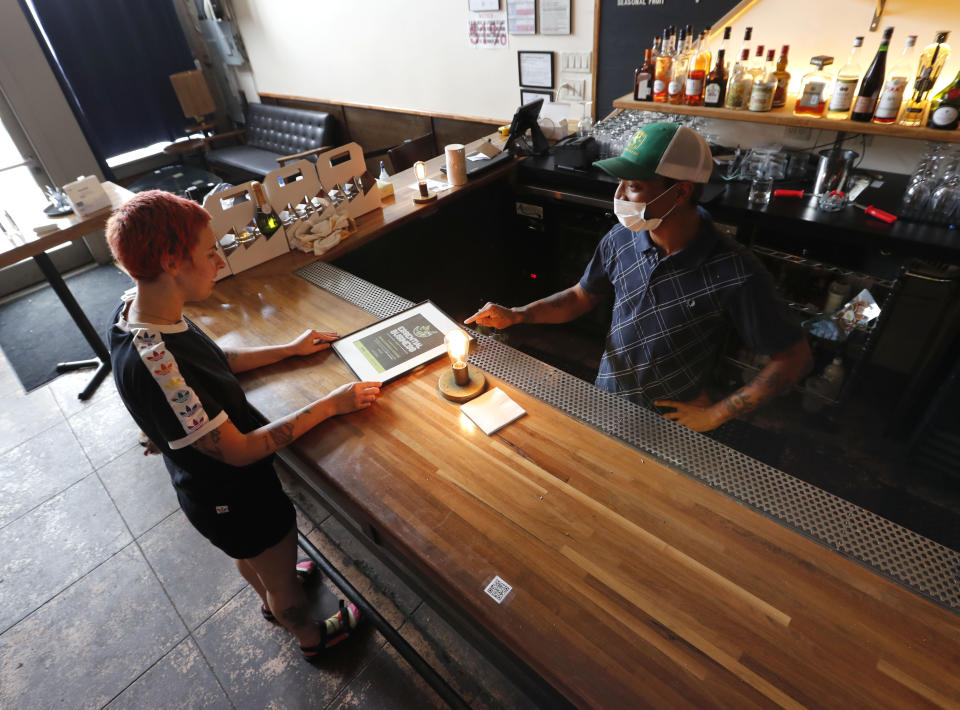 Omar Yeefoon, owner of Shoals Sound & Service vegan restaurant shows his sous chef Lauren Belmore an award from PETA they received, Tuesday, June 30, 2020, in Dallas. Yeefoon reopened his Dallas restaurant June 10 to "a pretty good reception," after having been shuttered for three months. The comeback was fleeting. After four days, Yeefoon had to shut down again in the face of a COVID-19 resurgence in Texas and lay off two of the four workers he'd brought back. (AP Photo/LM Otero)