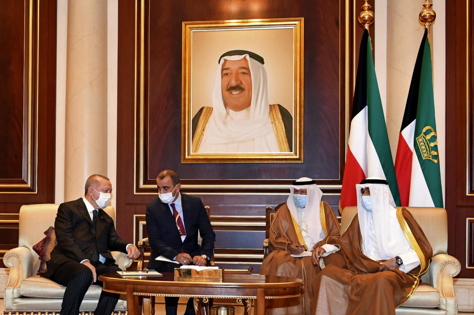 In this photo released by Kuwait News Agency, KUNA, Turkish President Recep Tayyip Erdogan, left, talks to Sheikh Nawaf al-Ahmad al-Sabah, the new Emir of Kuwait, right, in Kuwait, Wednesday, Oct. 7, 2020. The new emir replaced his half-brother, the late ruler Sheikh Sabah al-Ahmad al-Jaber al-Sabah, seen in portrait, who died in the United States at the age of 91 last month. (KUNA via AP)