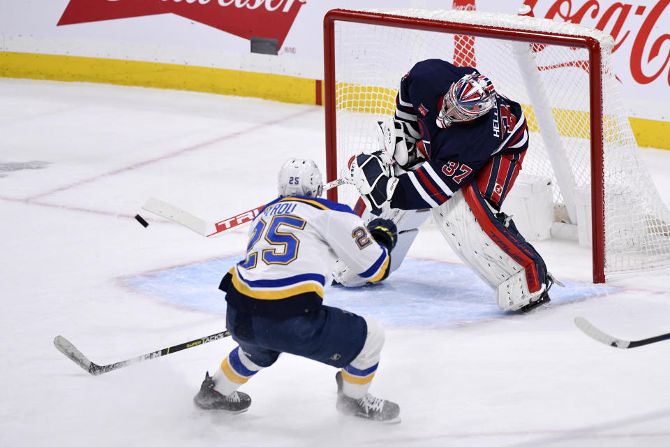 Winnipeg Jets goaltender Connor Hellebuyck (37) attempts a shot on the empty net as St. Louis Blues' Jordan Kyrou (25) skates toward him during third-period NHL hockey game action in Winnipeg, Manitoba, Monday, Jan. 30, 2023. (Fred Greenslade/The Canadian Press via AP)