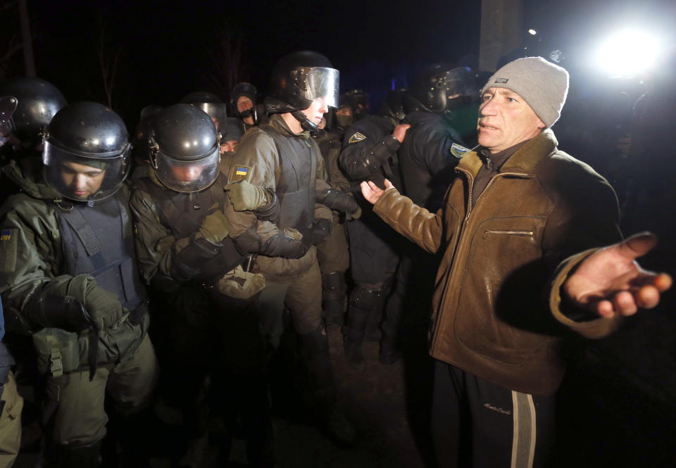 Protesters, who planned to stop buses carrying passengers evacuated from the Chinese city of Wuhan, speak to Ukrainian riot police blocking the road outside Novi Sarzhany, Ukraine, Thursday, Feb. 20, 2020. Several hundred residents in Ukraine's Poltava region protested to stop officials from quarantining the evacuees in their village because they feared becoming infected. Demonstrators put up road blocks and burned tires, while Ukrainian media reported that there were clashes with police, and more than 10 people were detained. (AP Photo/Efrem Lukatsky)