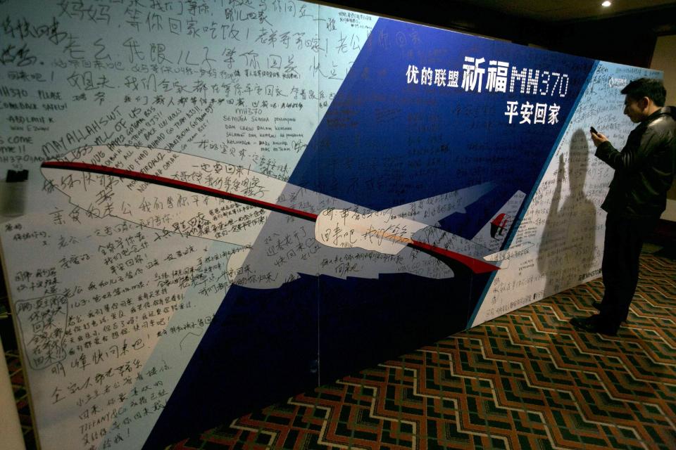 A man uses his mobile phone near a board with the characters "Pray for MH370 safe return" meant for relatives and workers to write their prayers and well wishes on in a room reserved for relatives of Chinese passengers aboard the missing Malaysia Airline jet in Beijing, China, Monday, March 24, 2014. Rain was expected to hamper the hunt Monday for debris suspected of being from the missing Malaysia Airlines jet, as the United States prepared to move a specialized device that can locate black boxes into the south Indian Ocean region. (AP Photo/Ng Han Guan)