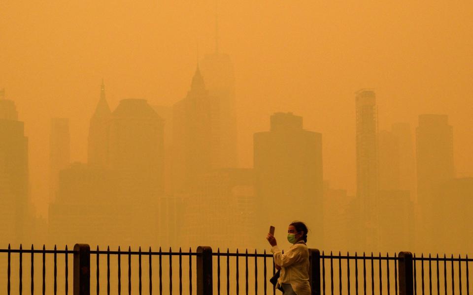 A person wearing a face mask takes photos of the skyline as smoke from wildfires in Canada cause hazy conditions in New York City - ANGELA WEISS/AFP