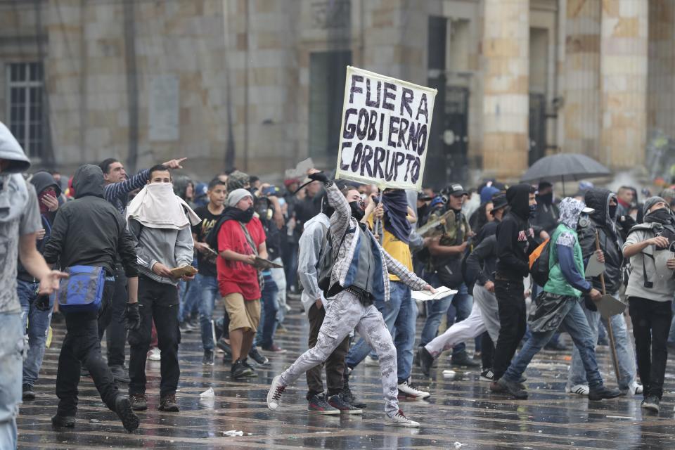 Anti-government protesters clash with the police during a nationwide strike, at Bolivar square in downtown Bogota, Colombia, Thursday, Nov. 21, 2019. Colombia's main union groups and student activists called for a strike to protest the economic policies of Colombian President Ivan Duque government and a long list of grievances. The sing held by the demonstrator reads in English "Corrupt governmetn out." (AP Photo/Fernando Vergara)