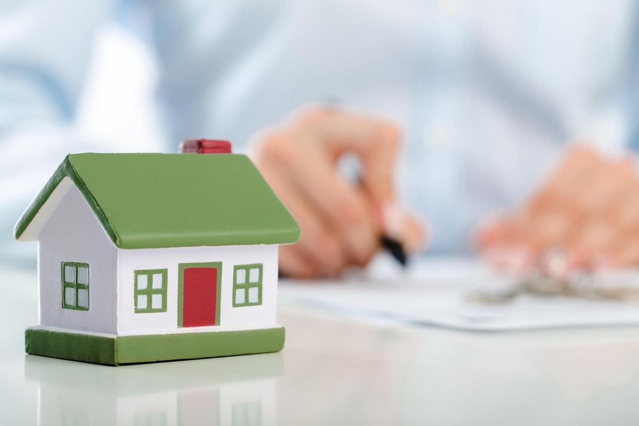 mini house with person signing mortgage in background