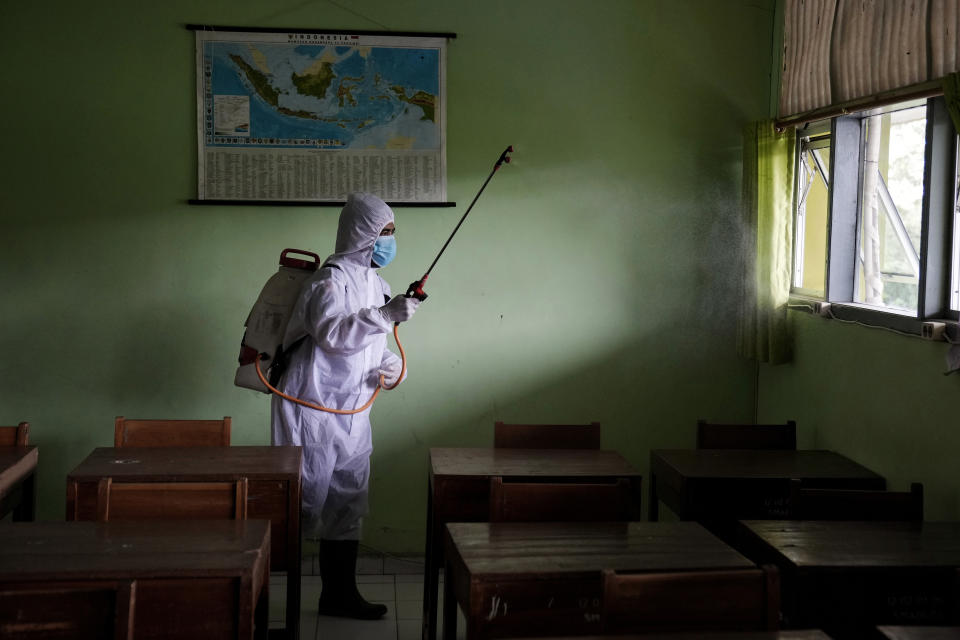 A Red Cross worker sprays disinfectant inside an empty classroom during the suspension of activities after a case of COVID-19 is found at a high school in Jakarta, Indonesia, Friday, Jan. 28, 2022. Dozens of schools in the capital city were temporarily closed following the findings of coronavirus cases among students and staff. (AP Photo/Dita Alangkara)