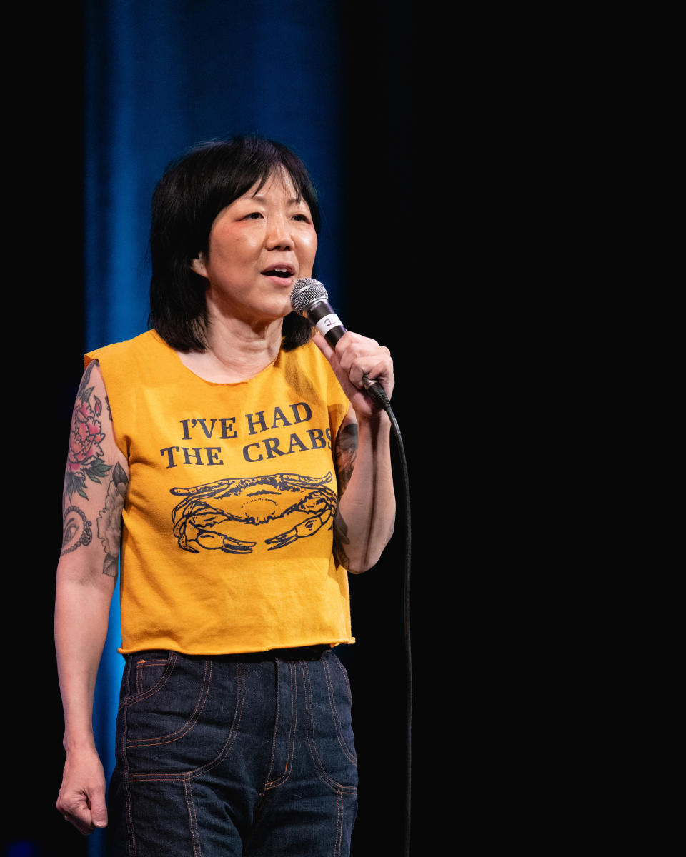 Woman performing stand-up comedy wearing a graphic tee and jeans